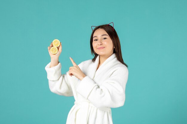 front view young female in bathrobe holding sliced lemons on blue background