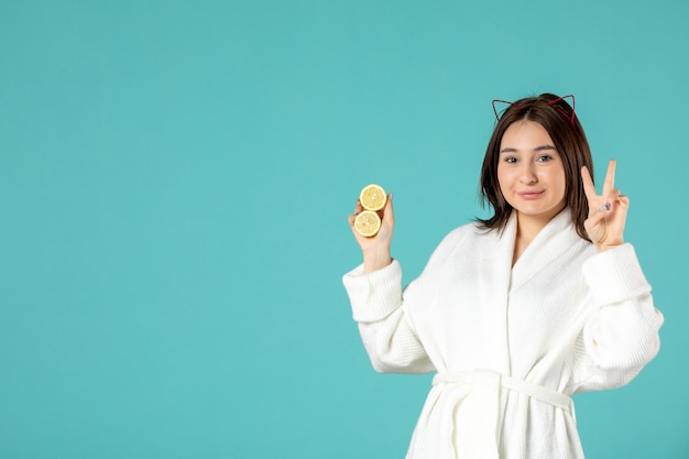 front view young female in bathrobe holding sliced lemons on blue background