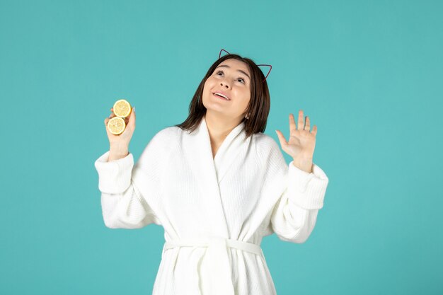 front view young female in bathrobe holding sliced lemons on blue background