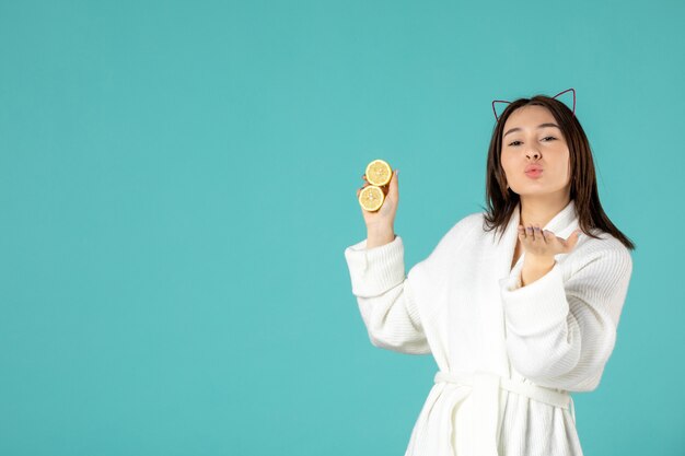 front view young female in bathrobe holding sliced lemons on blue background