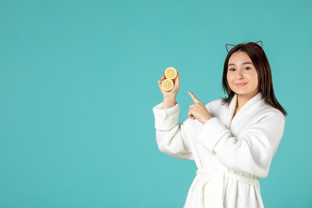 front view young female in bathrobe holding sliced lemons on blue background