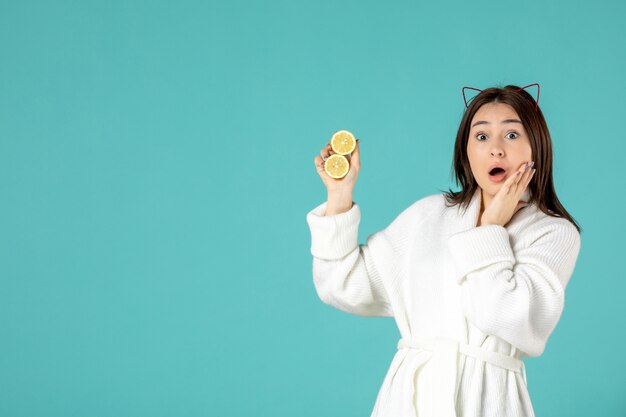 front view young female in bathrobe holding sliced lemons on blue background