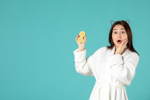 вид спереди молодая женщина в халате держит нарезанные лимоны на синем фоне