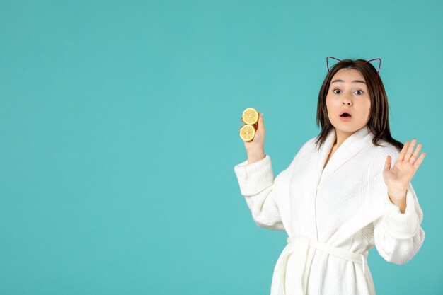 front view young female in bathrobe holding sliced lemons on blue background