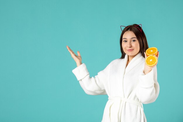 вид спереди молодая женщина в халате держит нарезанный апельсин на синем фоне душ красота массаж кожи женщина маска уход за собой поцелуй спа