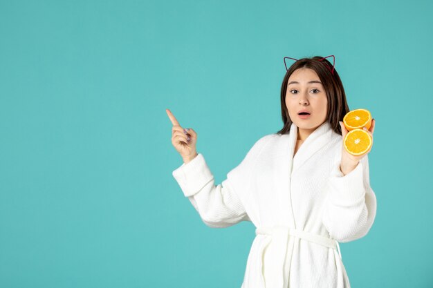 вид спереди молодая женщина в халате держит нарезанный апельсин на синем фоне