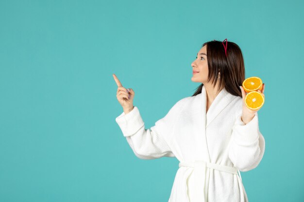 front view young female in bathrobe holding sliced orange on blue background