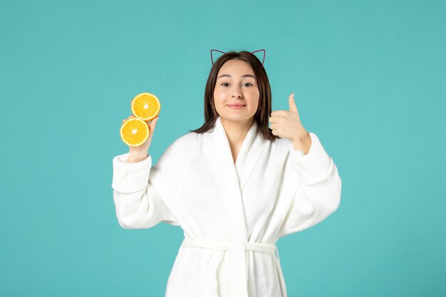 front view young female in bathrobe holding sliced orange on blue background