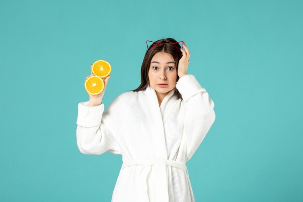 front view young female in bathrobe holding sliced orange on blue background