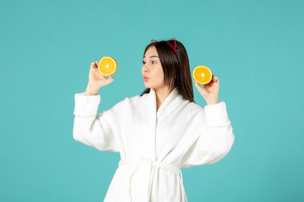 front view young female in bathrobe holding sliced orange on blue background