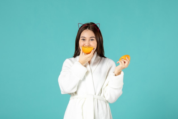 front view young female in bathrobe holding sliced orange on blue background
