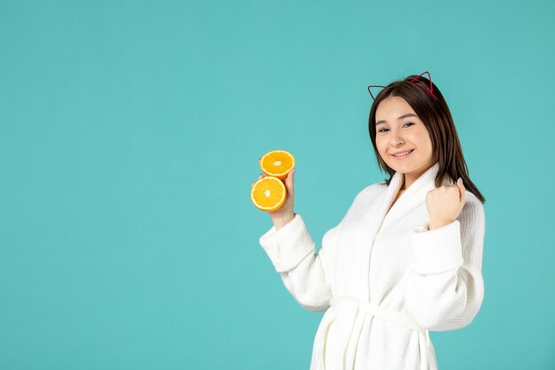 front view young female in bathrobe holding sliced orange on blue background