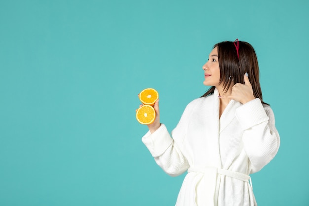 front view young female in bathrobe holding sliced orange on blue background