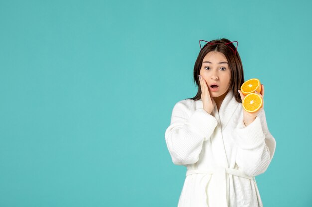 front view young female in bathrobe holding sliced orange on blue background