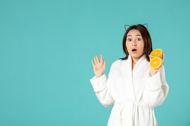 вид спереди молодая женщина в халате держит нарезанный апельсин на синем фоне