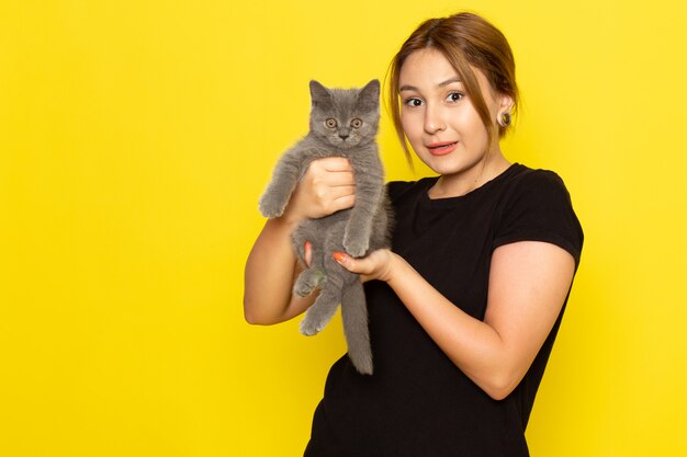 A front view young female in black dress holding cute little kitten on yellow