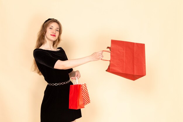 A front view young female in black dress with chain belt holding shopping packages on beige