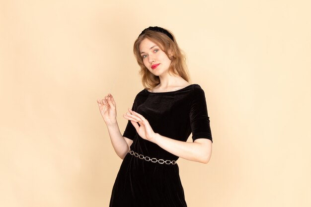 A front view young female in black dress with chain belt working with her nails on beige