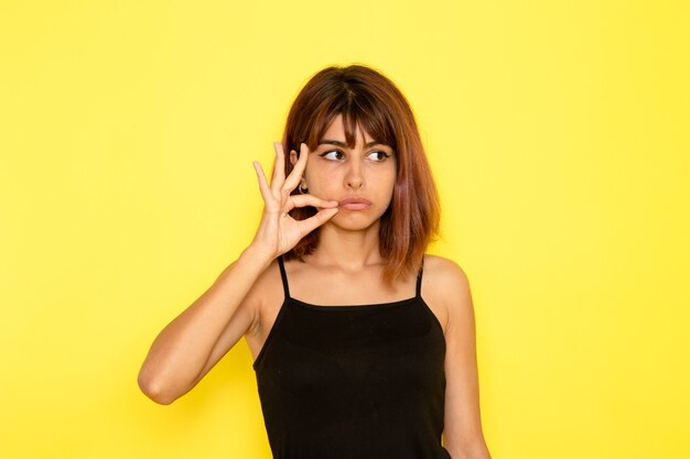 Front view of young female in black shirt and grey jeans just posing on yellow wall