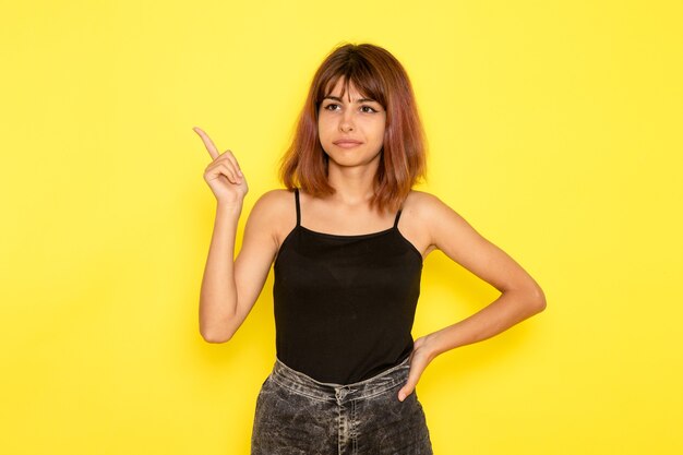 Front view of young female in black shirt and grey jeans posing on yellow desk model girl emotions color pose camera