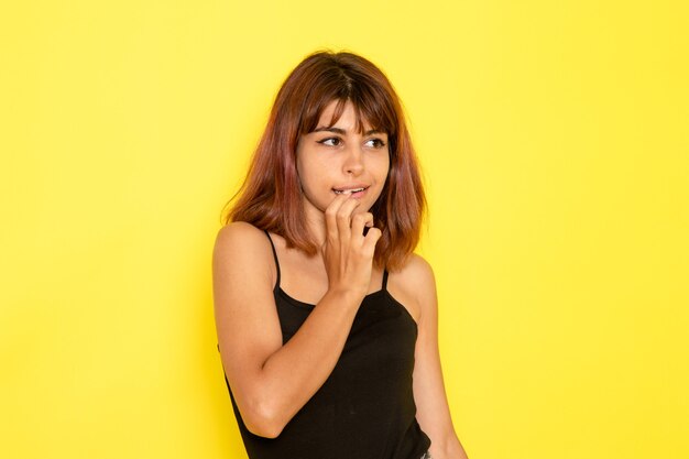Front view of young female in black shirt and grey jeans posing on yellow wall