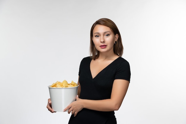 Front view young female in black shirt holding potato chips and posing on white surface