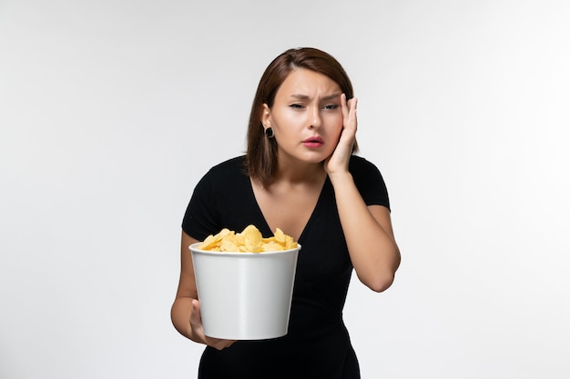 Вид спереди молодая женщина в черной рубашке держит картофельные чипсы и смотрит фильм на белой поверхности