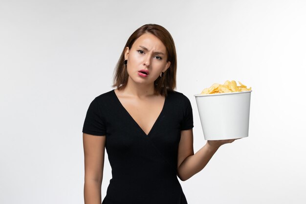 Вид спереди молодая женщина в черной рубашке, держащая картофельные чипсы на белом столе