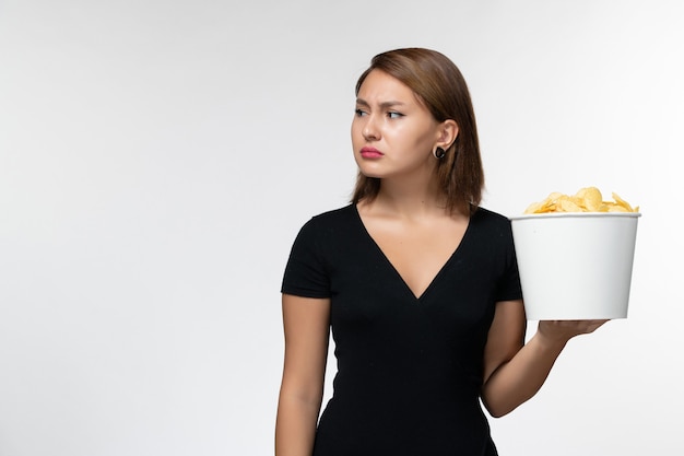 Вид спереди молодая женщина в черной рубашке, держащая картофельные чипсы на белой поверхности