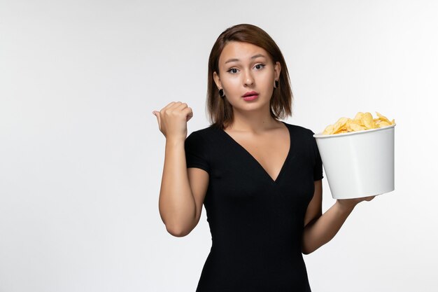 Вид спереди молодая женщина в черной рубашке, держащая картофельные чипсы на белой поверхности