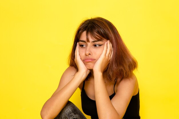 Front view of young female in black shirt posing with stressed expression on light yellow wall