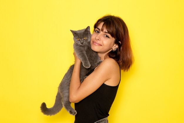 黄色の壁に子猫を保持して笑っている黒いシャツの若い女性の正面図