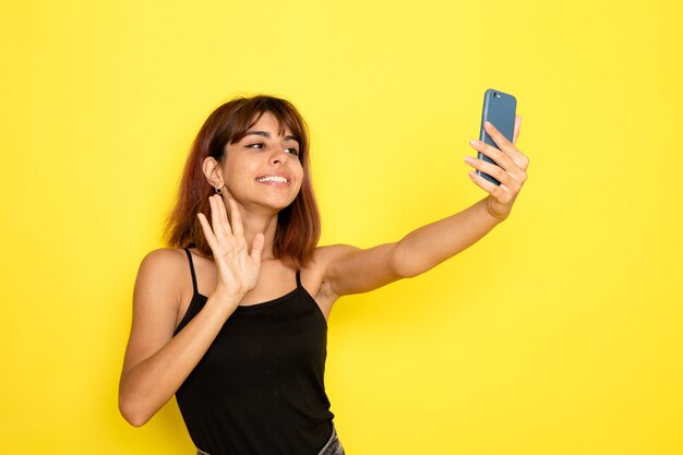 Front view of young female in black shirt taking selfie on yellow wall