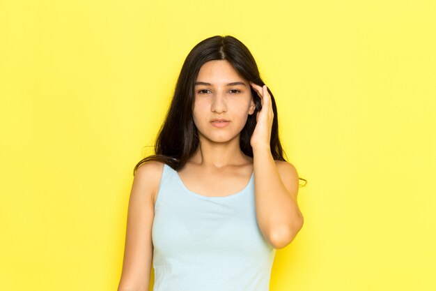 A front view young female in blue shirt having a headache on the yellow background girl pose model beauty young