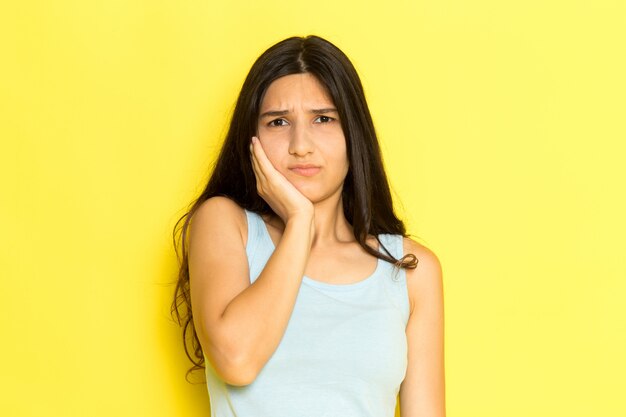 A front view young female in blue shirt having a toothache on the yellow background girl pose model beauty young