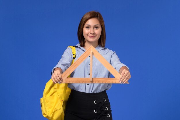 Front view of young female in blue shirt holding wooden triangle smiling on the blue wall