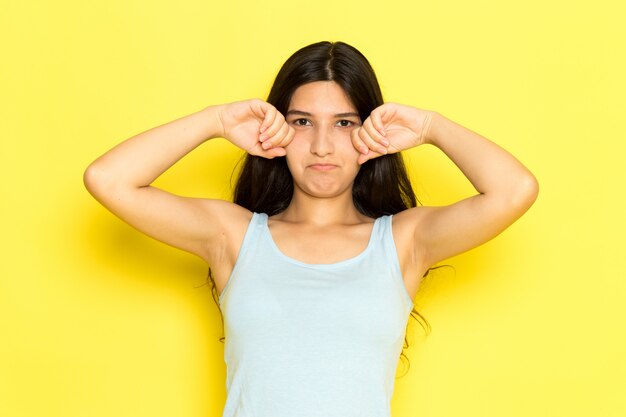 A front view young female in blue shirt posing and fake crying on the yellow background girl pose model beauty young
