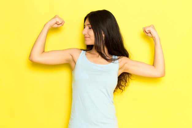 Free photo a front view young female in blue shirt posing and flexing with smile on the yellow background girl pose model beauty young