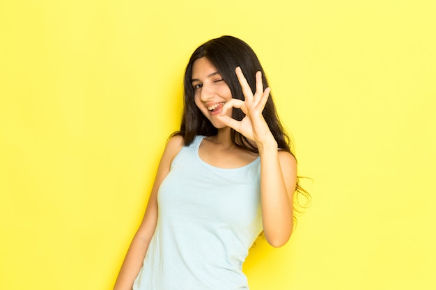 A front view young female in blue shirt posing smiling and showing alright sign