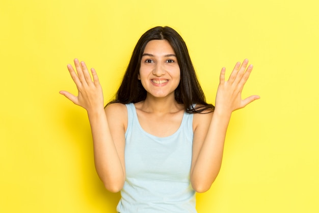 A front view young female in blue shirt posing with happy expression on the yellow background girl pose model beauty young