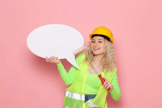 緑の建設スーツヘルメットの正面の若い女性ビルダーピンクのスペースアーキテクチャ建設仕事仕事女性にわずかな笑顔で白い記号でちょうどポーズ