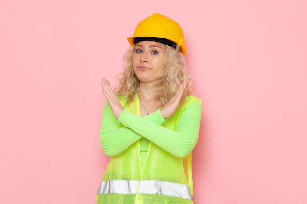 ピンクのスペース建築工事の禁止標識を示す緑の建設スーツヘルメットで正面の若い女性ビルダー