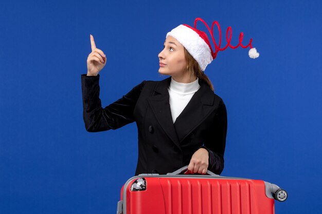 Вид спереди молодая женщина, несущая большую красную сумку на синей стене, отпуск, поездка, женщина, отдых