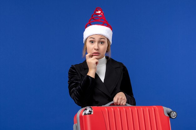 Вид спереди молодая женщина, несущая красную сумку на синем полу, праздник, отпуск, поездка, женщина