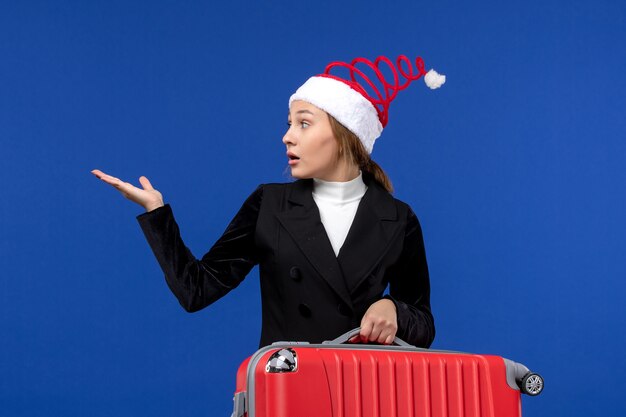 Вид спереди молодая женщина, несущая красную сумку на синей стене, поездка, отпуск, отпуск, женщина