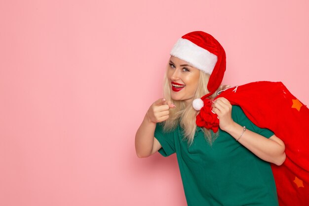 Front view young female carrying red bag with presents on pink wall holiday model xmas new year color photo santa