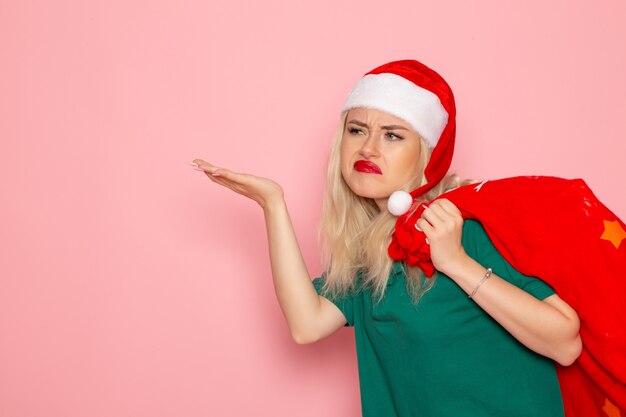 Front view young female carrying red bag with presents on pink wall model xmas new year color santa holiday