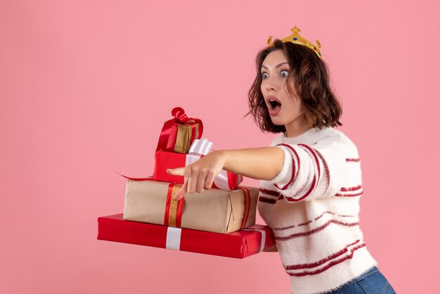 正面図クリスマスを運ぶ若い女性はピンクの背景に彼女の頭に王冠を提示しますクリスマス休暇感情女性新年の色