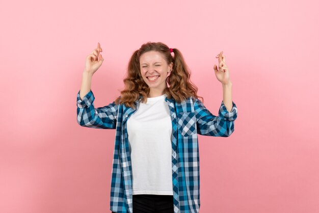 ピンクの背景の女性の若者の色の感情の子供モデルでポーズをとって指を交差させる市松模様のシャツを着た若い女性の正面図