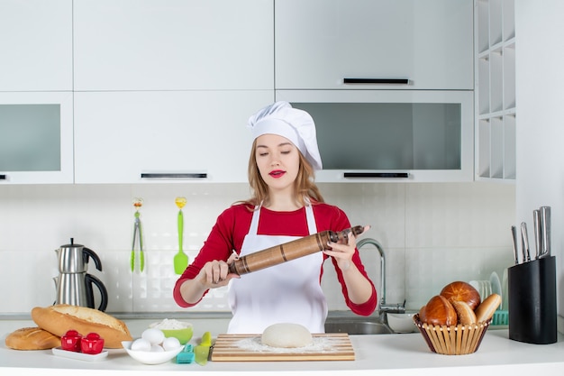 Front view young female chef holding up rolling pin in the kitchen